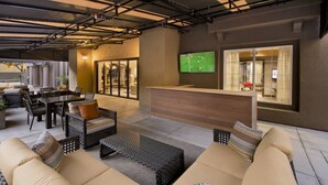 A modern lounge area with a sofa, chairs, a table, and a TV screen displaying a soccer game. - Bluebird Suites in Santa Clara (Santa Clara)