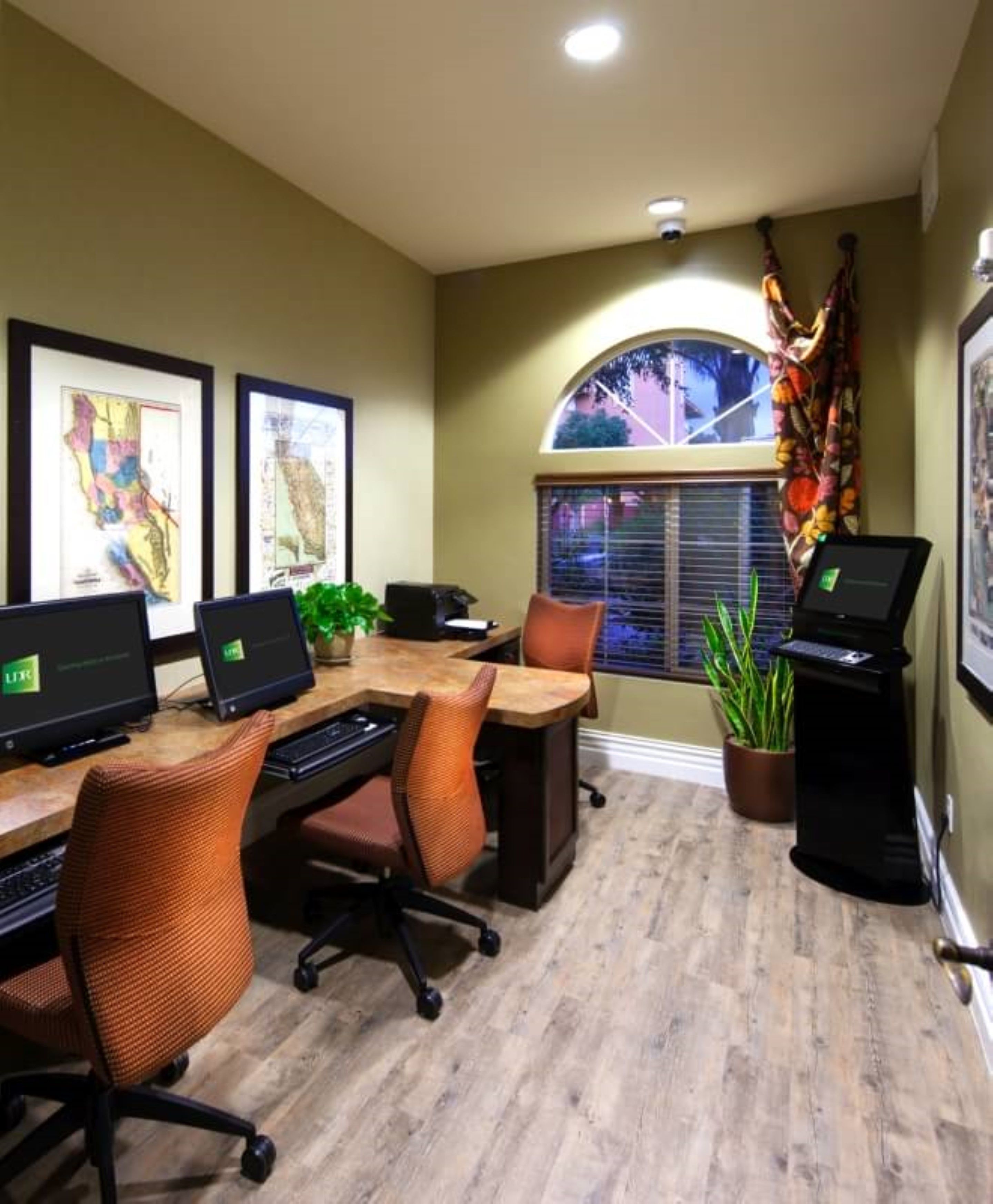 A conference room with a long table, four office chairs, two laptops, and two desktop computers.