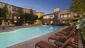 A swimming pool with lounge chairs and a building in the background. - Bluebird Suites in Santa Clara (Santa Clara)