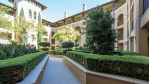 A courtyard with a central pathway flanked by neatly trimmed hedges and a building with balconies and arched windows. - Bluebird Suites in North San Jose (San Jose)