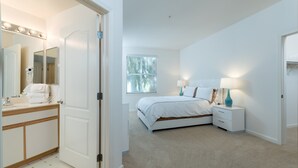 A bedroom with a bed, bedside table, lamp, and a window with blinds. - Bluebird Suites in North San Jose (San Jose)