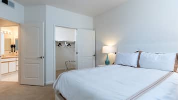A hotel room with a large bed, a walk-in closet, a bathroom with a vanity, and a nightstand with a lamp.