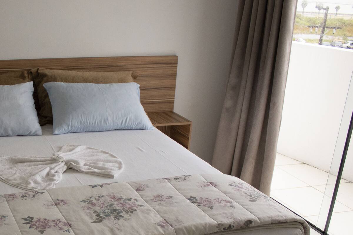 A neatly made bed with a floral bedspread, two pillows, and a folded towel on a wooden headboard.