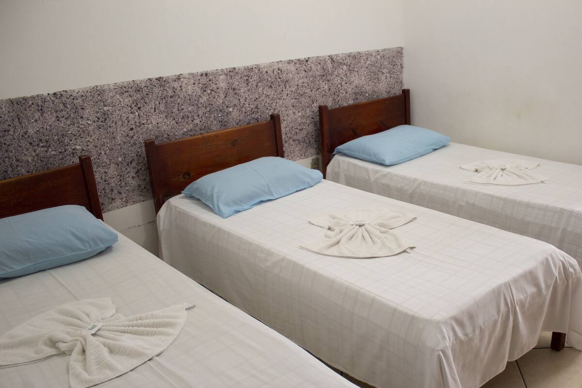 Three single beds with wooden headboards, each with a blue pillow and a white towel arranged on the bed.