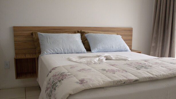Een opgemaakt bed met een bloemenbedekking en twee kussens, een houten hoofdbord en een nachtkastje met een lamp.