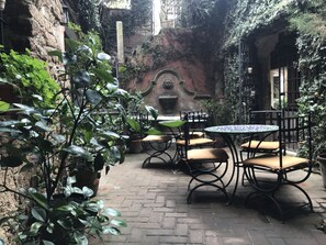 Une cour avec un sol en briques, des plantes en pot et du mobilier d’extérieur, notamment une table ronde et des chaises.