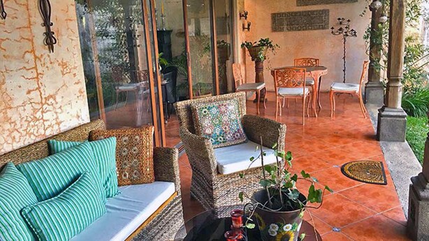 A cozy patio area with wicker furniture, a sofa with striped cushions, and a table with a potted plant.