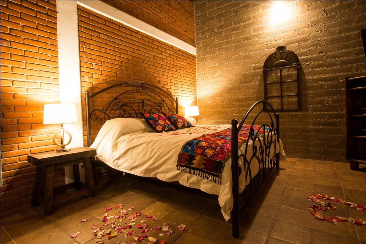 A bed with a metal frame, a wooden nightstand, and a brick wall.