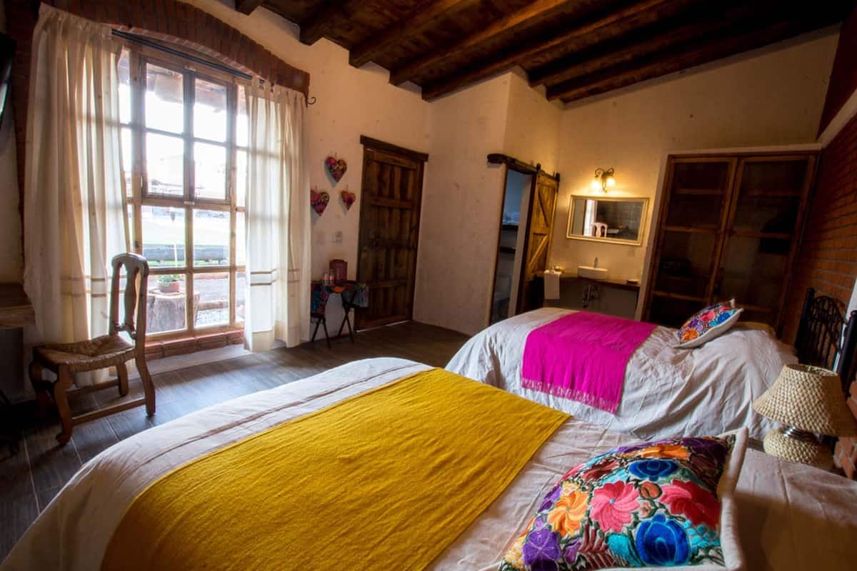 A bedroom with two beds, a wooden chair, a small table, and a window with curtains.