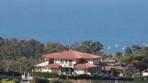 Casa de dos pisos con techo rojo, rodeada de vegetación y con vista a un cuerpo de agua con barcos.