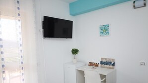 Una habitación pequeña y luminosa con un escritorio blanco, un televisor de pantalla plana en la pared, una planta pequeña en maceta y un letrero motivacional.
