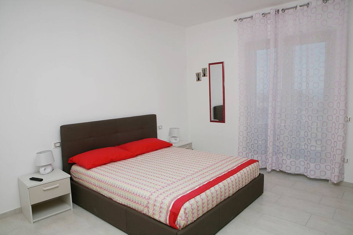 A bedroom with a bed, nightstands, a mirror, and a window with curtains.