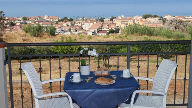 Un balcón con una mesa lista para dos personas, con vistas a un pueblo costero.
