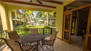 A balcony with a round table and four chairs, overlooking a pool and greenery. - Club del cielo Unit 1 (Jacó)