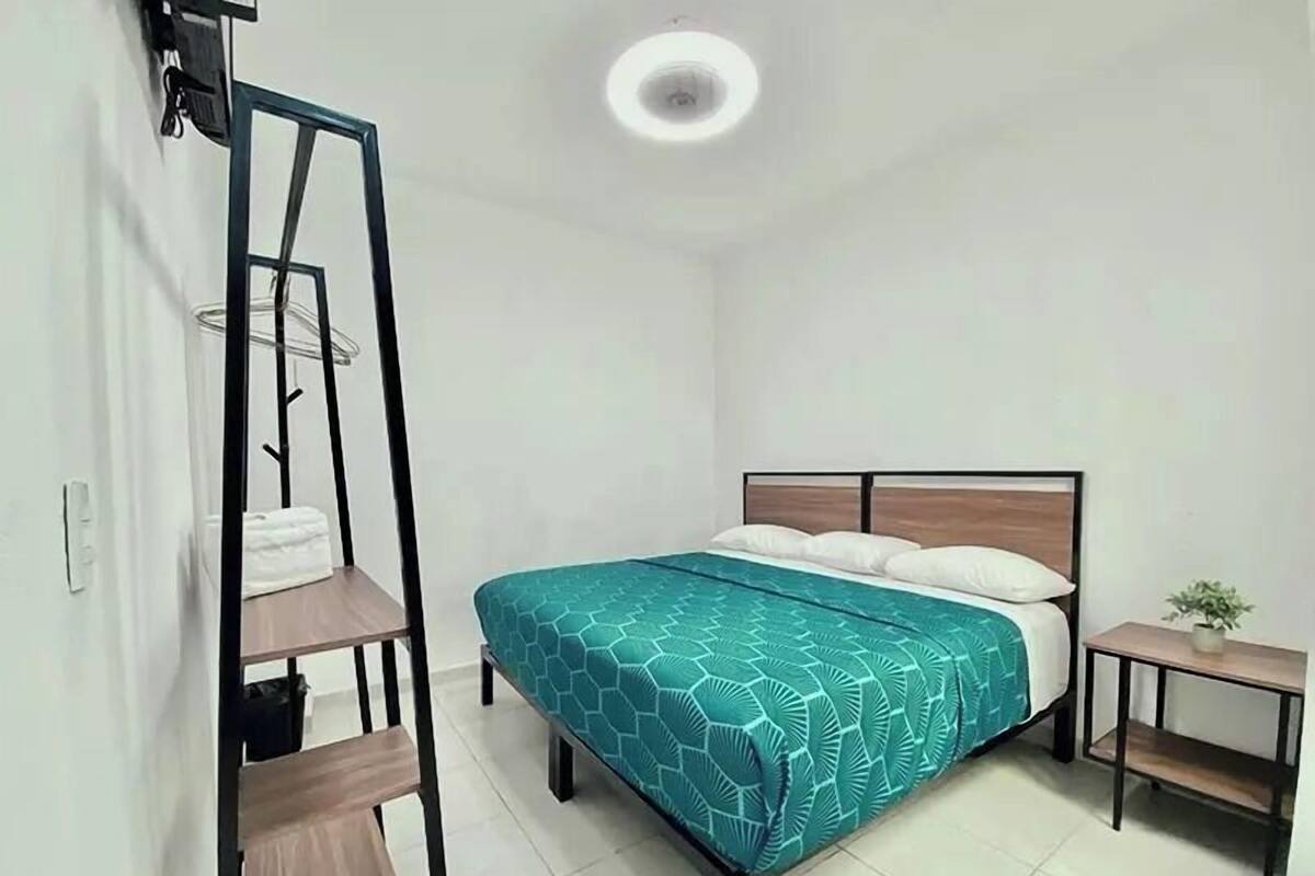 Un dormitorio con cama, mesita de noche, una silla colgante y una pequeña mesa con una planta.