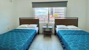 A hotel room with two beds, a small table, and a window with a city view. - Casa Zapopan Hotel (Zapopan)