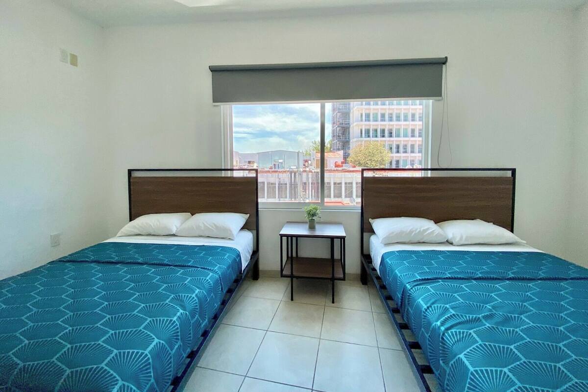 Habitación de hotel con dos camas, una mesita y una ventana con vistas a la ciudad.