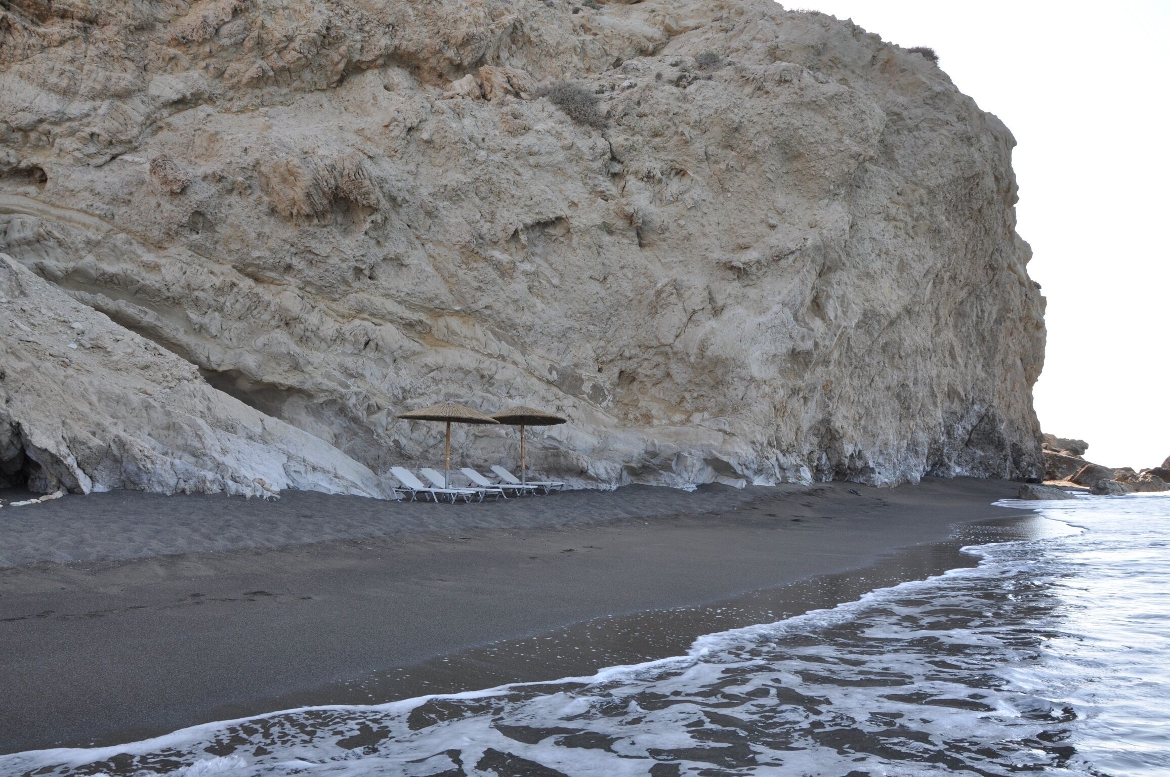 Une plage avec une falaise rocheuse, des chaises longues et des parasols.