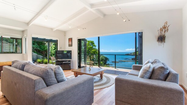 Ein modernes Wohnzimmer mit grauen Sofas, einem Holztisch und einem großen Fenster mit Meerblick.