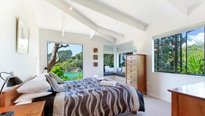 Ein modernes Schlafzimmer mit einem großen Bett, einem Schreibtisch und einer Kommode. Ein Fenster bietet Blick auf Grünflächen.