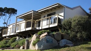 A two-story building with a balcony, supported by large rocks, and a sign indicating it is a heritage site. - KINGFISHER COTTAGE Beachfront at Bay of Fires (Bay of Fires)