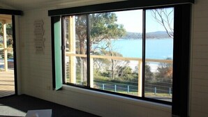 A room with a large window offering a view of a body of water and trees. - KINGFISHER COTTAGE Beachfront at Bay of Fires (Bay of Fires)