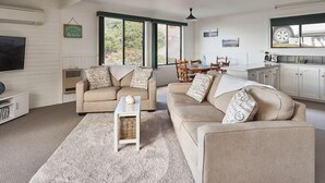 A spacious living room with a large window, a dining area, and a kitchen. - KINGFISHER COTTAGE Beachfront at Bay of Fires (Bay of Fires)