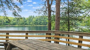 Um deck de madeira com bancos oferece vista para um lago, cercado por árvores.
