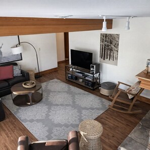 A modern living room with a flat-screen TV, wooden furniture, a patterned rug, and a painting on the wall.