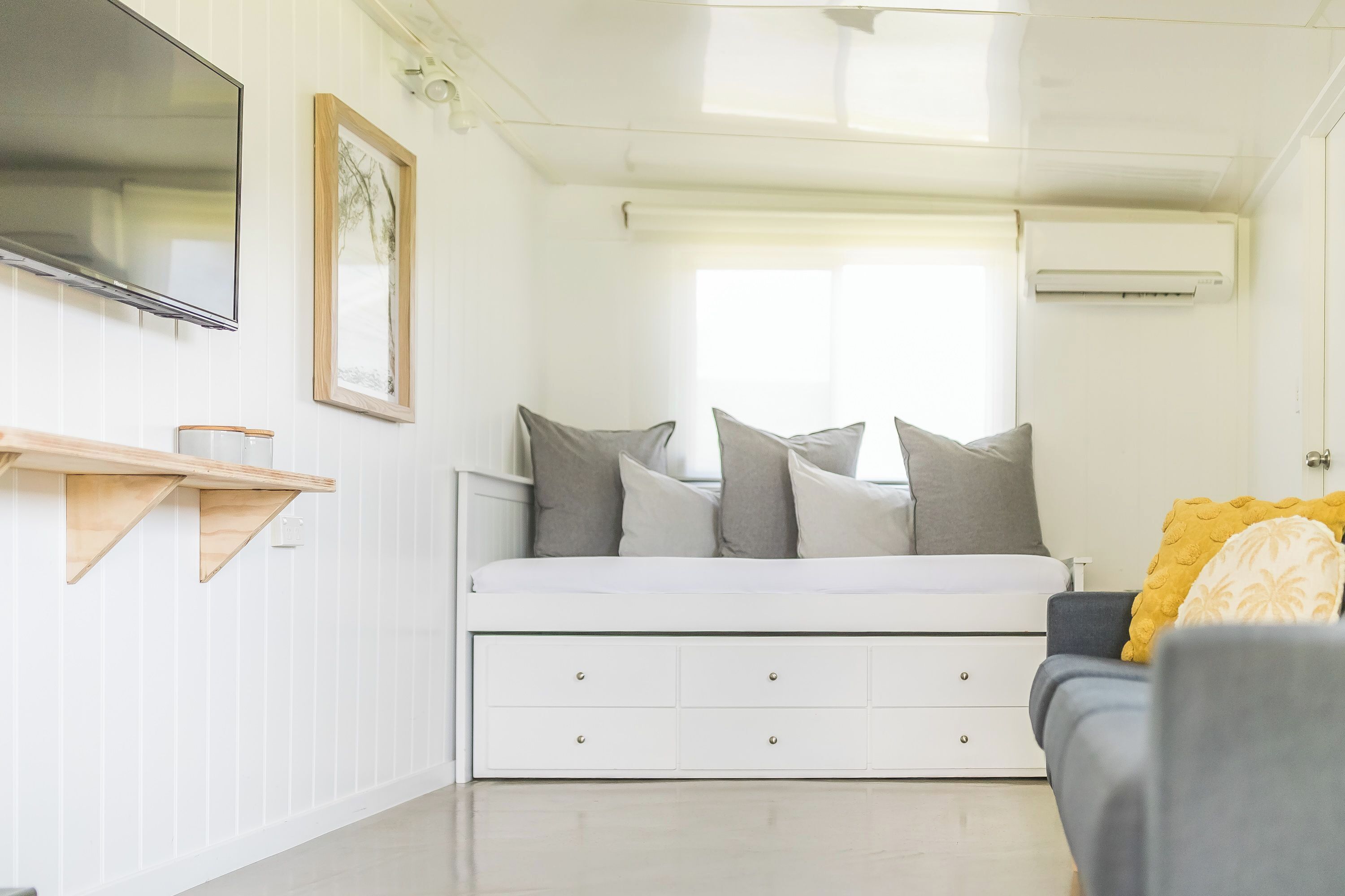 Une chambre moderne et bien éclairée, équipée d’un lit, d’un téléviseur fixé au mur et d’une fenêtre avec des stores.