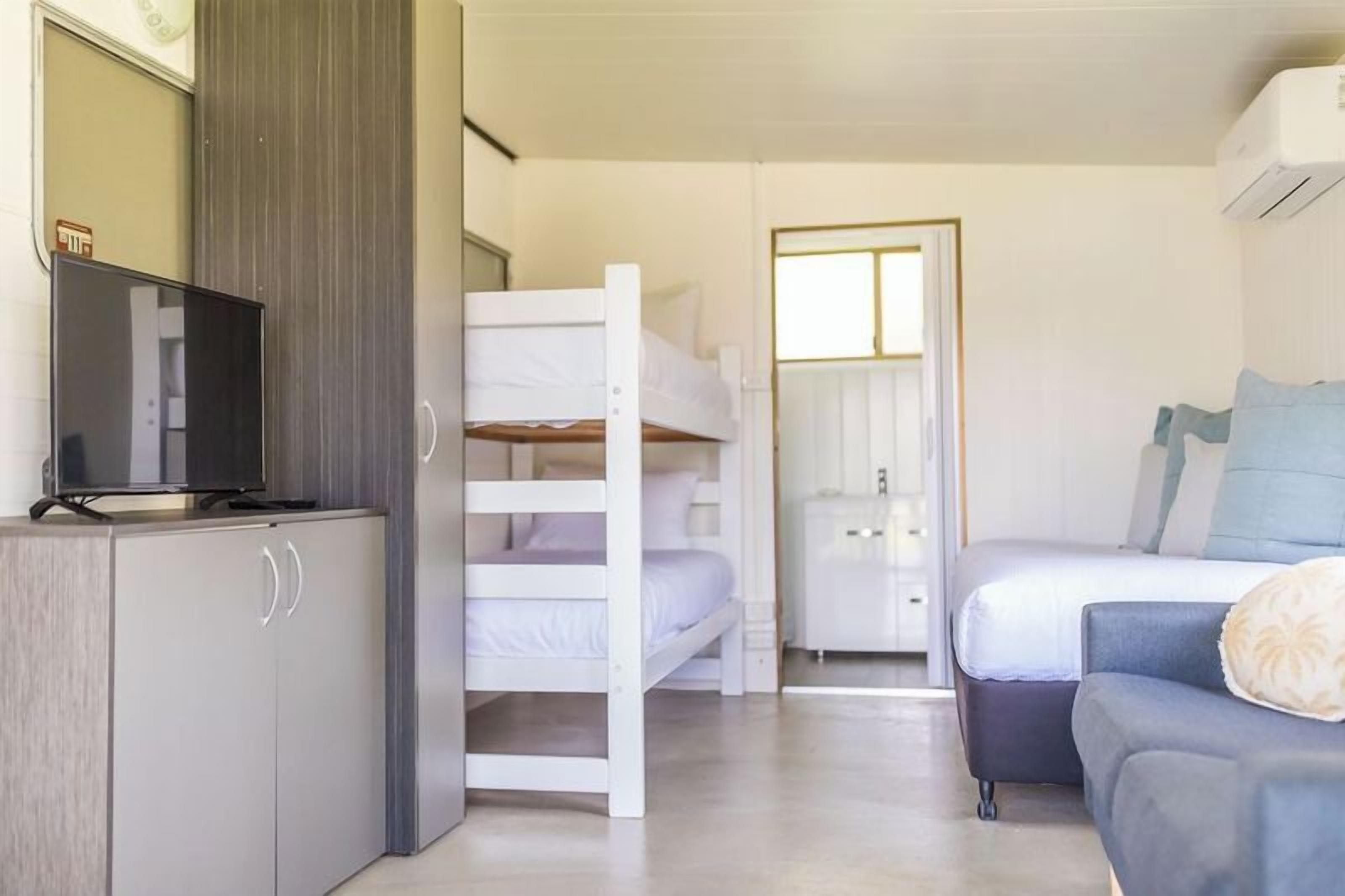 Une chambre d’hôtel avec un lit superposé, un canapé, une télévision et une armoire.