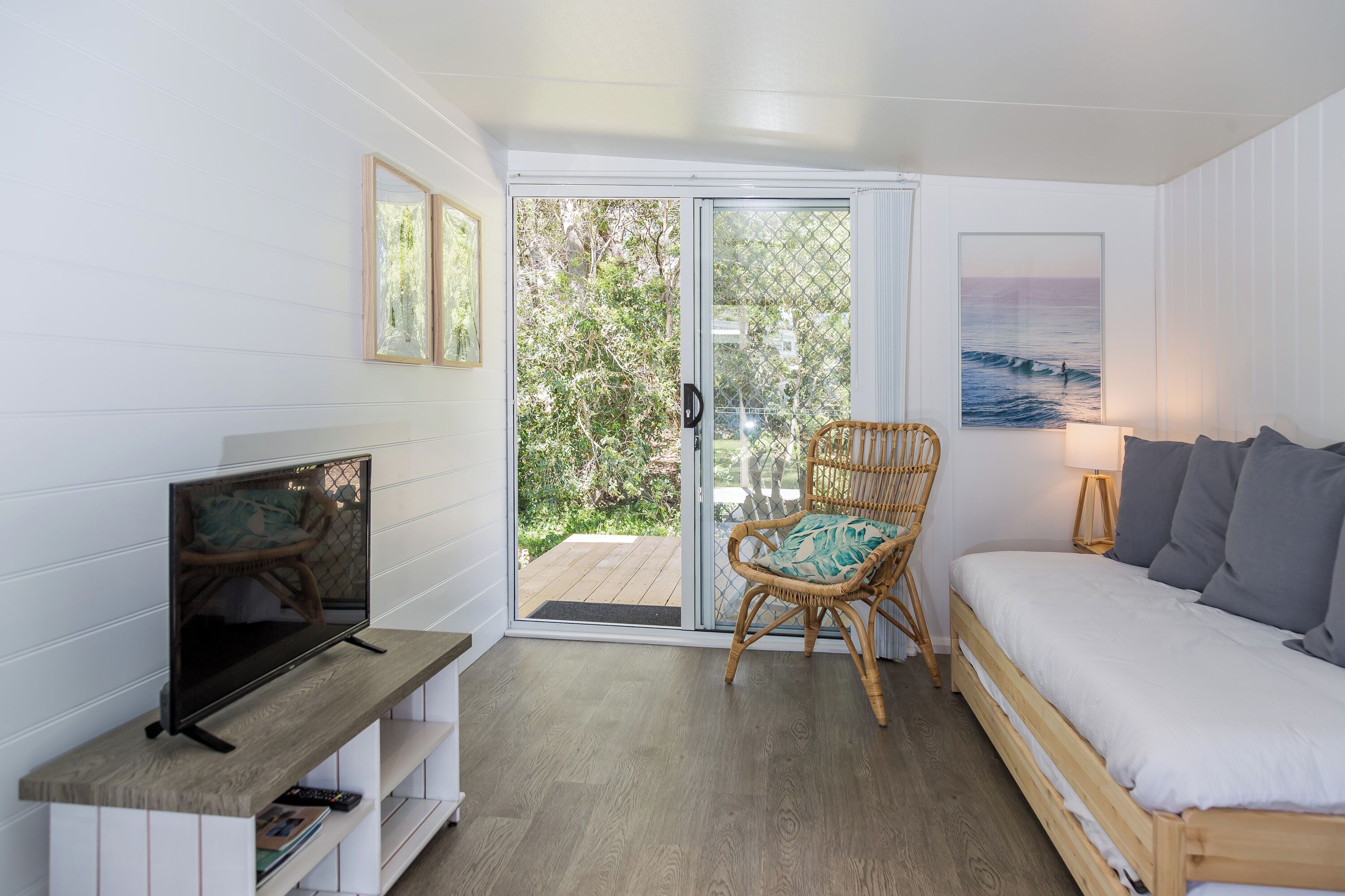 A room with a bed, a TV on a wooden stand, a wicker chair, and a sliding glass door leading to an outdoor area.