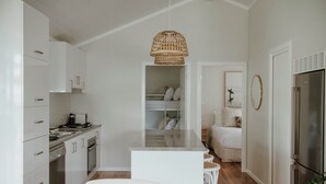 A modern kitchen with white cabinetry, a central island, and a hanging wicker light fixture. - Surfside Cudmirrah Beach (Cudmirrah)