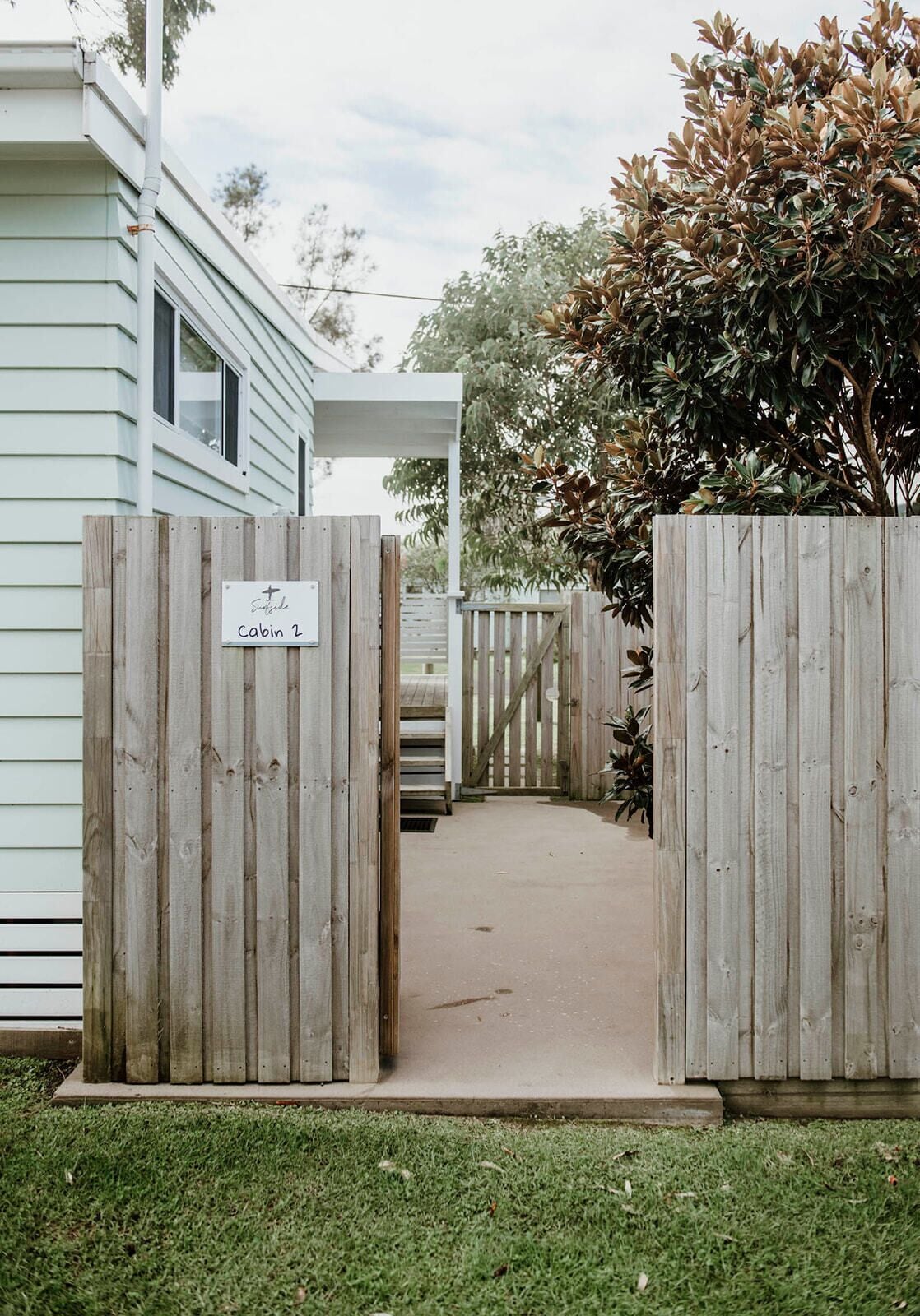 A wooden gate with a sign reading "Sunnyside Cabin 2" leading to a covered walkway.