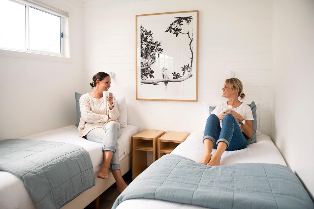 Two people sitting on separate beds in a room with a framed artwork on the wall.