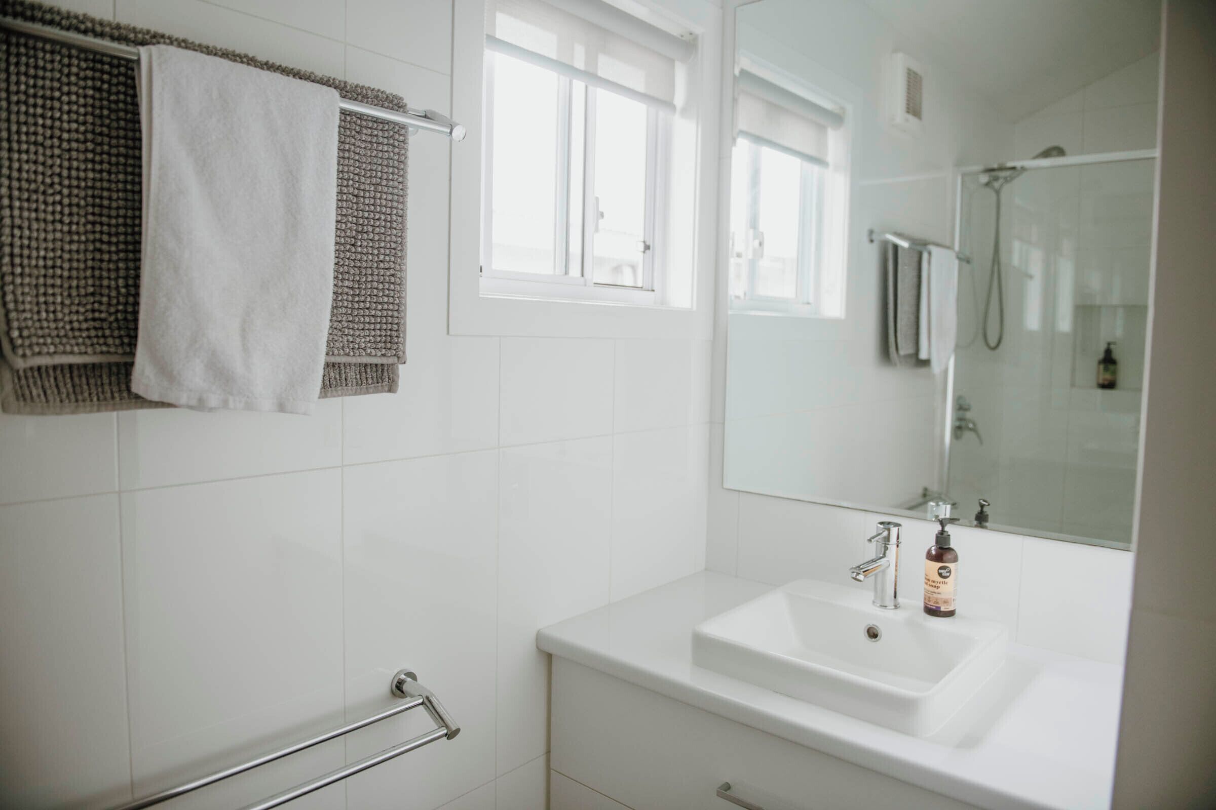 A modern bathroom with a white sink, a glass shower enclosure, and a towel rack with a white towel.