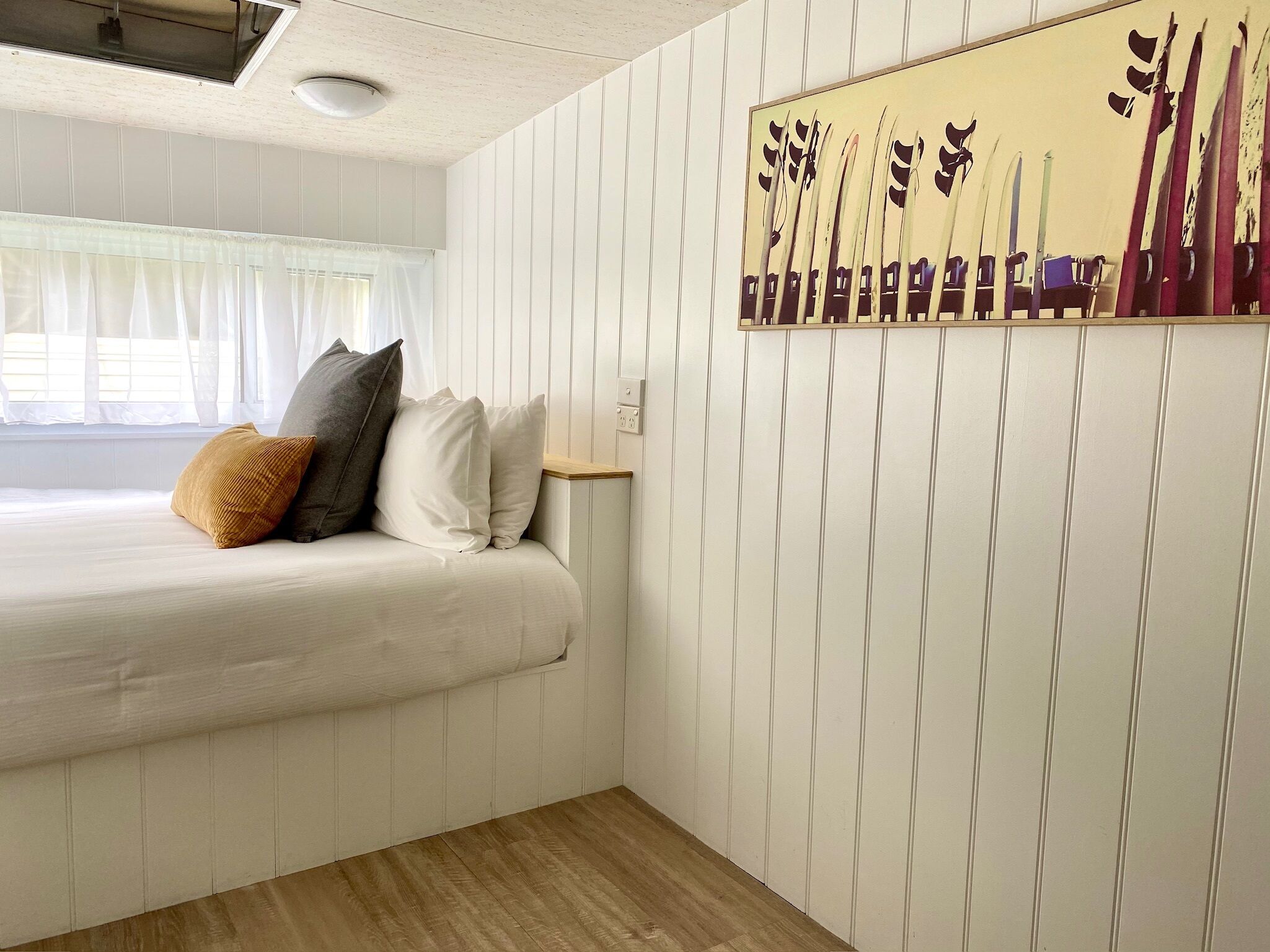 A hotel room with a bed, pillows, a painting of skis, and a wooden floor.