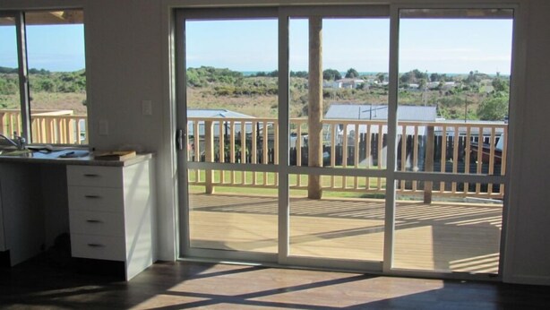 A room with a sliding glass door leading to an outdoor deck with a view of a residential area and hills.