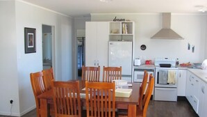 A compact kitchen with white cabinets, a white refrigerator, a stove, and a microwave. There is a dining table with wooden chairs.