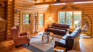 A log cabin interior with a wooden ceiling, a leather sofa, a glass coffee table, and a hanging chair. - Dancing Bear Lodge--Log Cabin Getaway (Fort Calhoun)