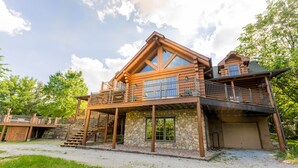A log cabin with a stone foundation, a wooden deck, and a garage. - Dancing Bear Lodge--Log Cabin Getaway (Fort Calhoun)