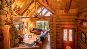 A log cabin interior with a stone wall, wooden beams, a fireplace, a sofa, and a dining table. - Dancing Bear Lodge--Log Cabin Getaway (Fort Calhoun)