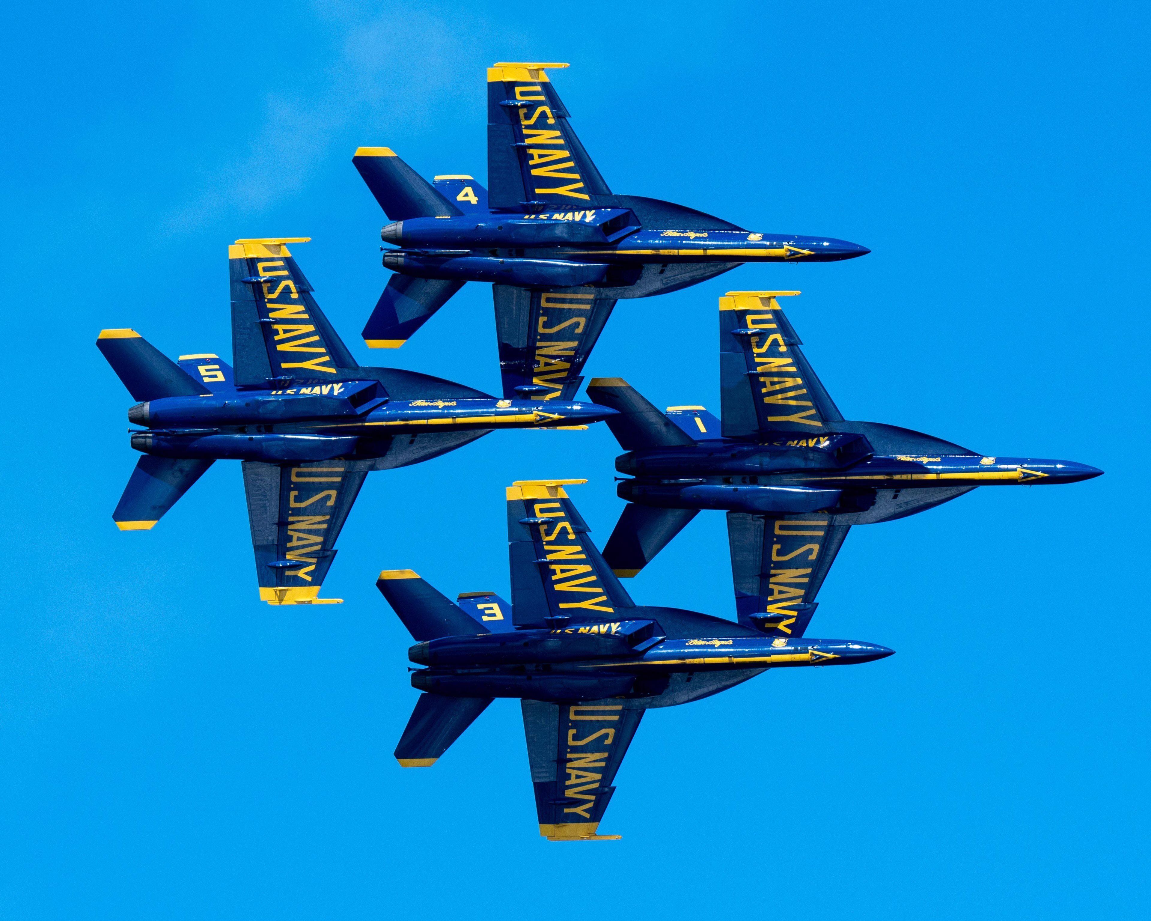 Four blue and yellow US Navy aircraft flying in formation against a clear blue sky.
