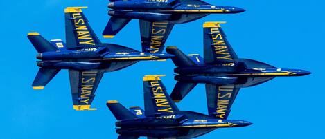 Four blue and yellow US Navy aircraft flying in formation against a clear blue sky.