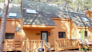 Une cabane en rondins à deux étages, dotée d’un porche à l’avant, d’une porte et de deux fenêtres.