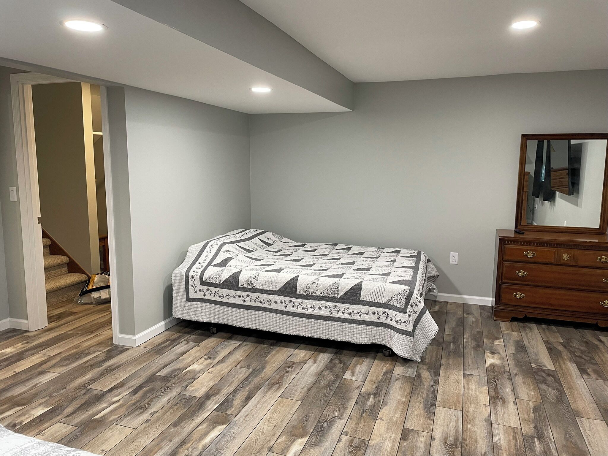 A bedroom with a bed, wooden flooring, a dresser, and a mirror.