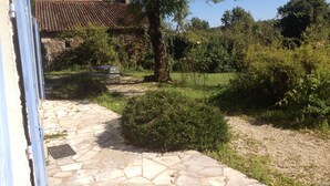 A stone pathway leading to a rustic building with a tiled roof, surrounded by lush greenery and a small garden area.