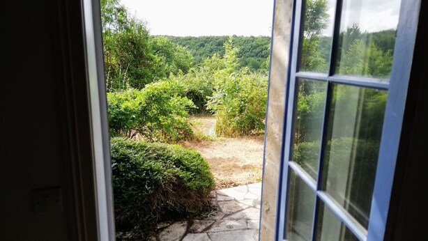A stone pathway leading to a lush garden with dense greenery and a hilly landscape in the background.