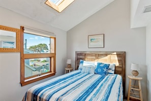 A bedroom with a large bed, a wooden headboard, two bedside tables, a nightstand, a framed picture, and a skylight.