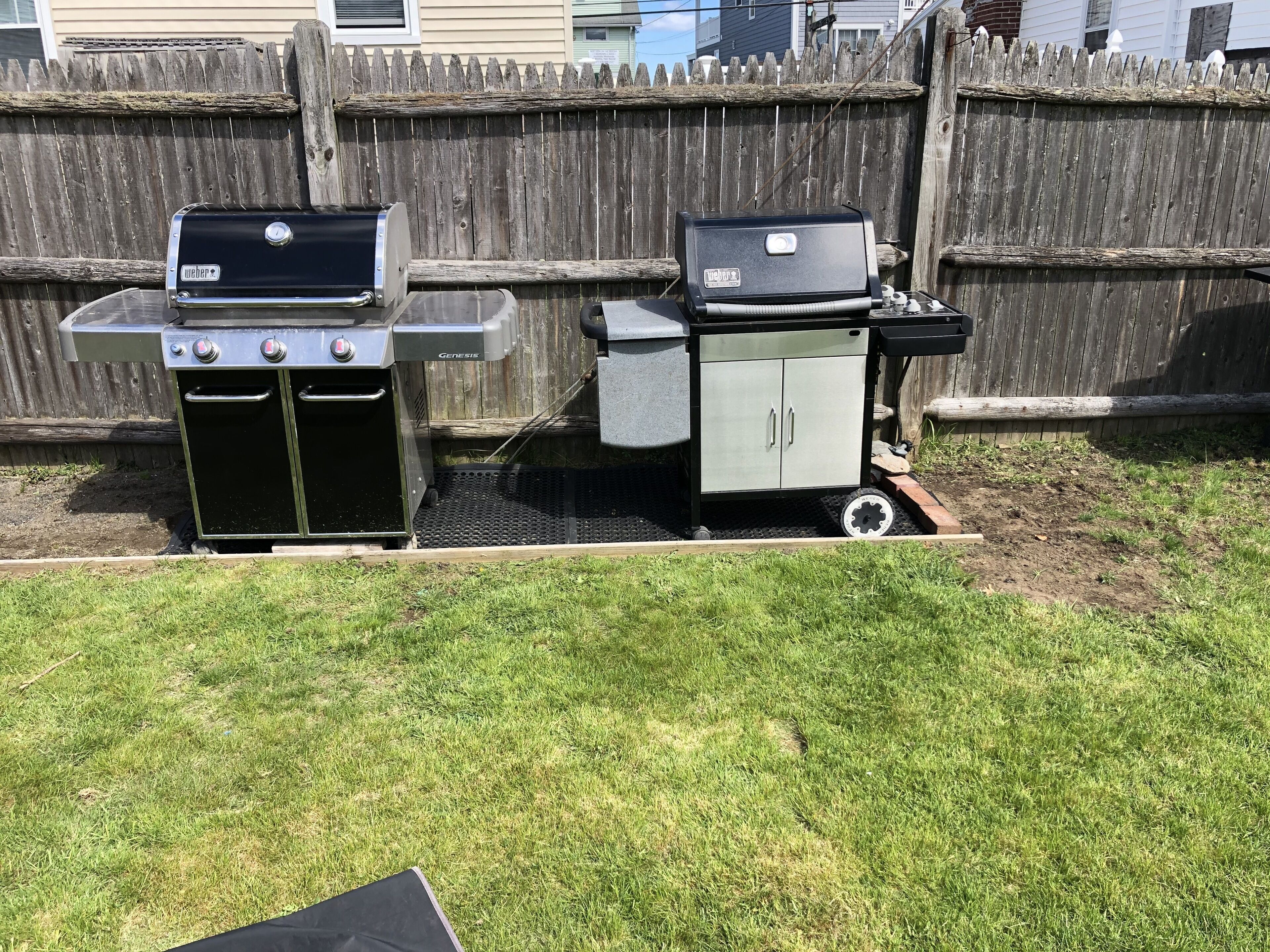 Un cortile con due barbecue Weber Genesis a gas e un armadietto contenitore.